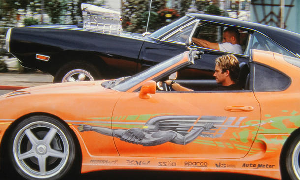 Paul Walker fährt in einem Auto, dahinter sieht man Vin Diesel in einem anderen Auto. Beide fahren auf der Straße, es ist ein Ausschnitt aus dem Film Fast & Furious.