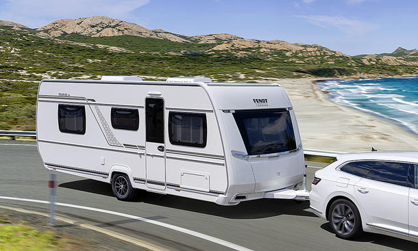 Das Bild zeigt den Fendt Tendenza (2025) von schräg vorne rechts fotografiert. Der Wohnwagen wird von einem VW Arteon an einem Stand vorbeigezogen.