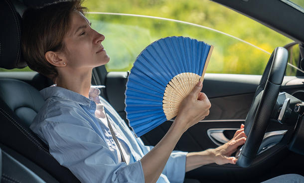 Eine Frau sitzt in einem heißen Fahrzeug und fächert sich Luft zu.