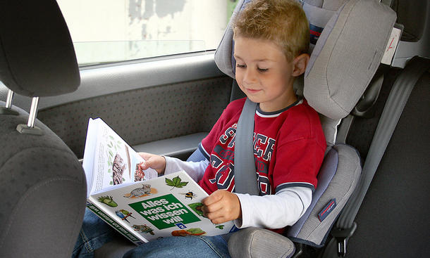 Ein Junge sitzt in einem Kindersitz im Auto und liest ein Buch.