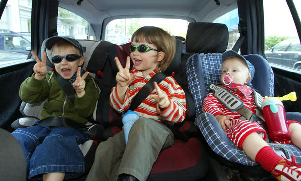 Drei Kinder sitzen nebeneinander im Auto auf der Rückbank auf verschiedenen Kindersitzen.