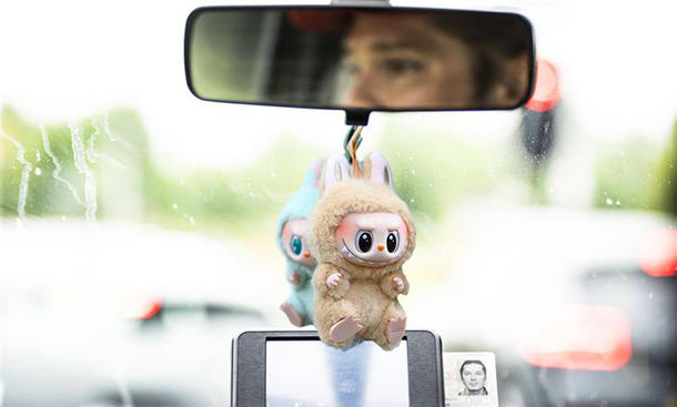 Zwei Labubu-Figuren hängen am Rückspiegel eines Autos.