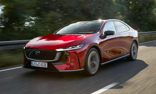 Der Mazda6e (2025) fährt über eine Landstraße, fotografiert von schräg vorne.