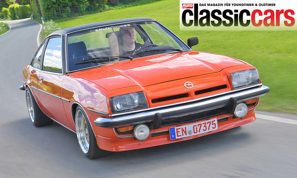 Der Opel Manta B 1.9 E fährt über eine Landstraße, von schräg vorne fotografiert.