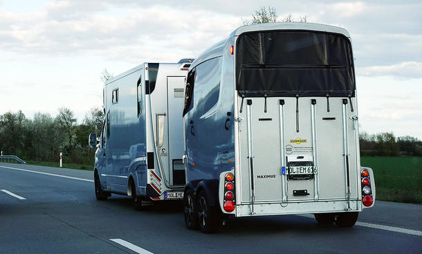 Ein Wohnmobil zieht einen Pferdeanhänger auf einer Straße.