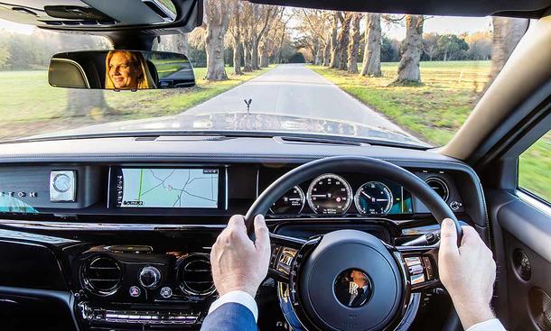 Rolls-Royce Chauffeur Academy: Das Bild zeigt die Ego-Perspektive am Steuer eines Rolls-Royce Phantom; im Rückspiegel ist eine Frau auf der Rücksitzbank zu sehen.