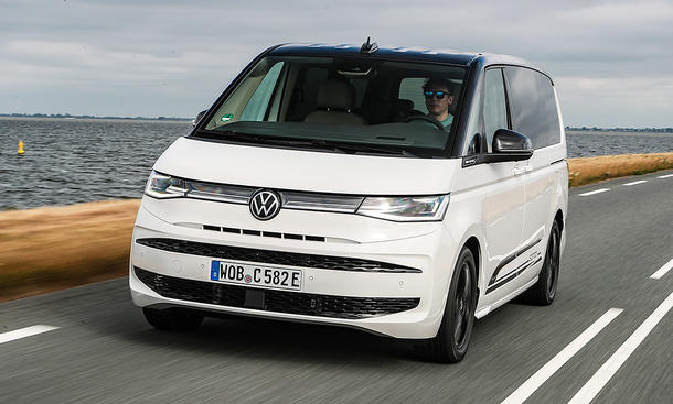 Der VW Multivan eHybrid 4Motion (2025) fährt über eine Landstraße, fotografiert von schräg vorne.