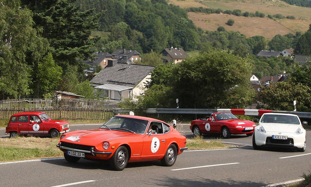 Viele bunte Autos bei der ersten Youngtimer Tour, hier ein orangefarbener Datsun 240Z vor einem Mazda MX-5 NA und einem Renault 