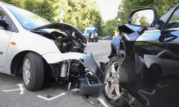 Unfall mit zwei Fahrzeugen auf einer Straße. Ein Polizeifahrzeug steht im Hintergrund.